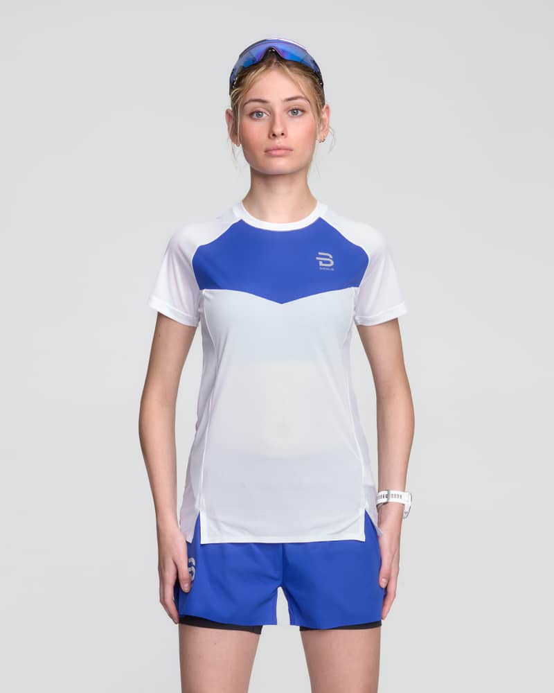Female runner in a white Dæhlie Run 365 t-shirt with blue chest panel for high-performance running.