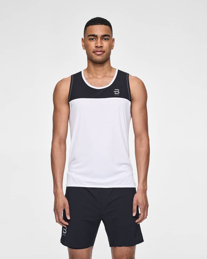 Man in a white Dæhlie Singlet Run 365 with black colorblocking, designed for optimal performance while running.