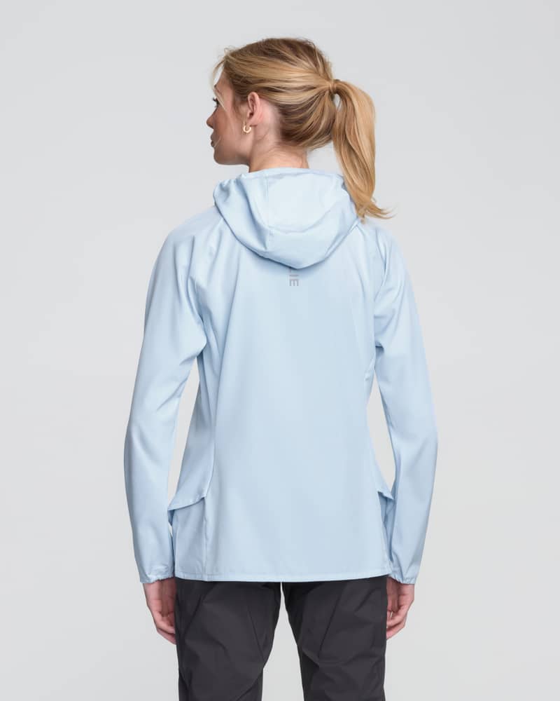Back view of a woman in the light sky blue Dæhlie Jacket Run 2.0 showing its athletic fit and hood.