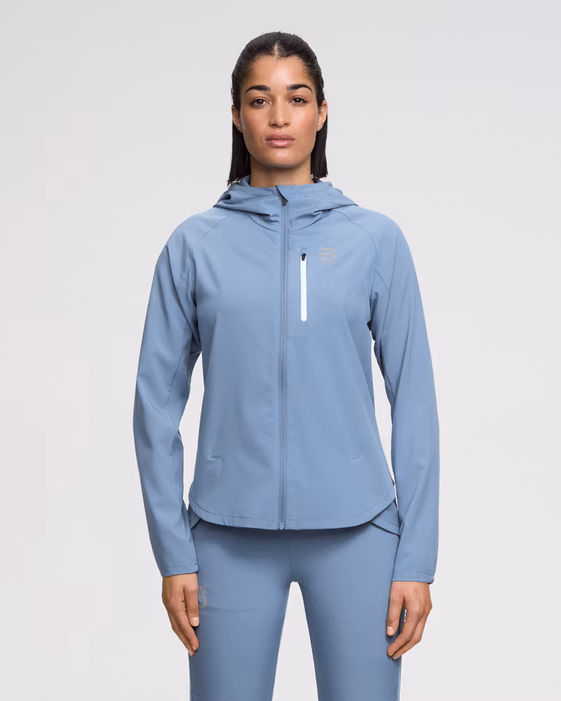 Front view of a model wearing the Dæhlie pastel blue Jacket Run 2.0 for women, with a fixed hood and front zipper chest pocket.