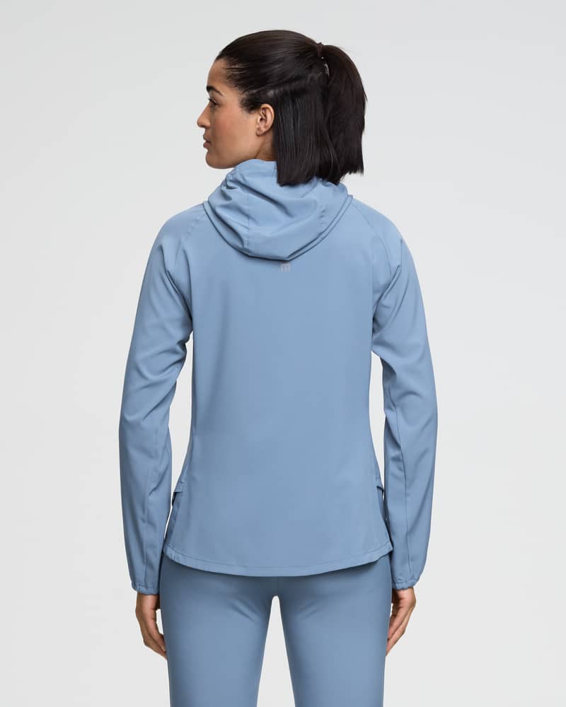 Back view of a female runner wearing the Dæhlie pastel blue running jacket, showing the split hem for easy movement.
