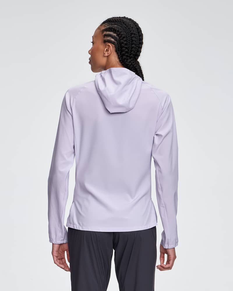 Back view of a woman wearing the lavender Dæhlie Jacket Run 2.0, showing the split hem for mobility.