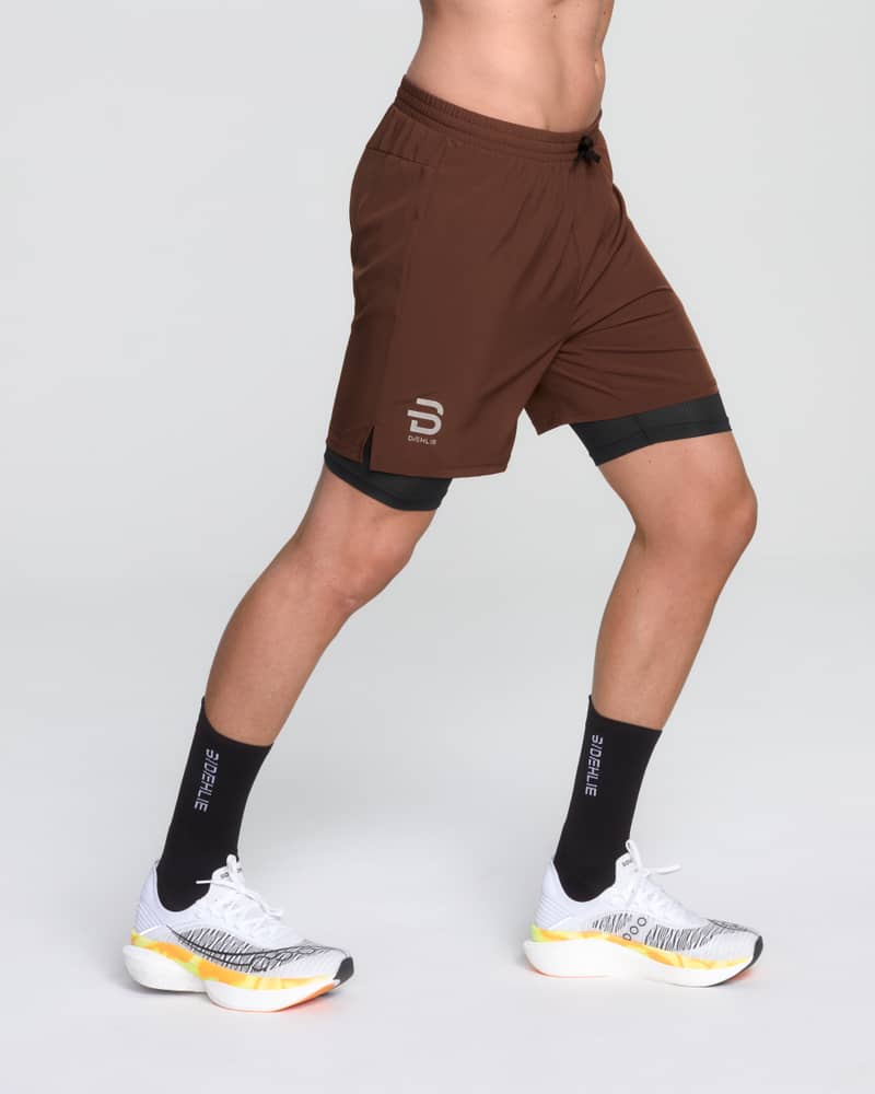 Runner's side view in Dæhlie's brown Shorts Run 2 in 1, featuring moisture-wicking fabric.