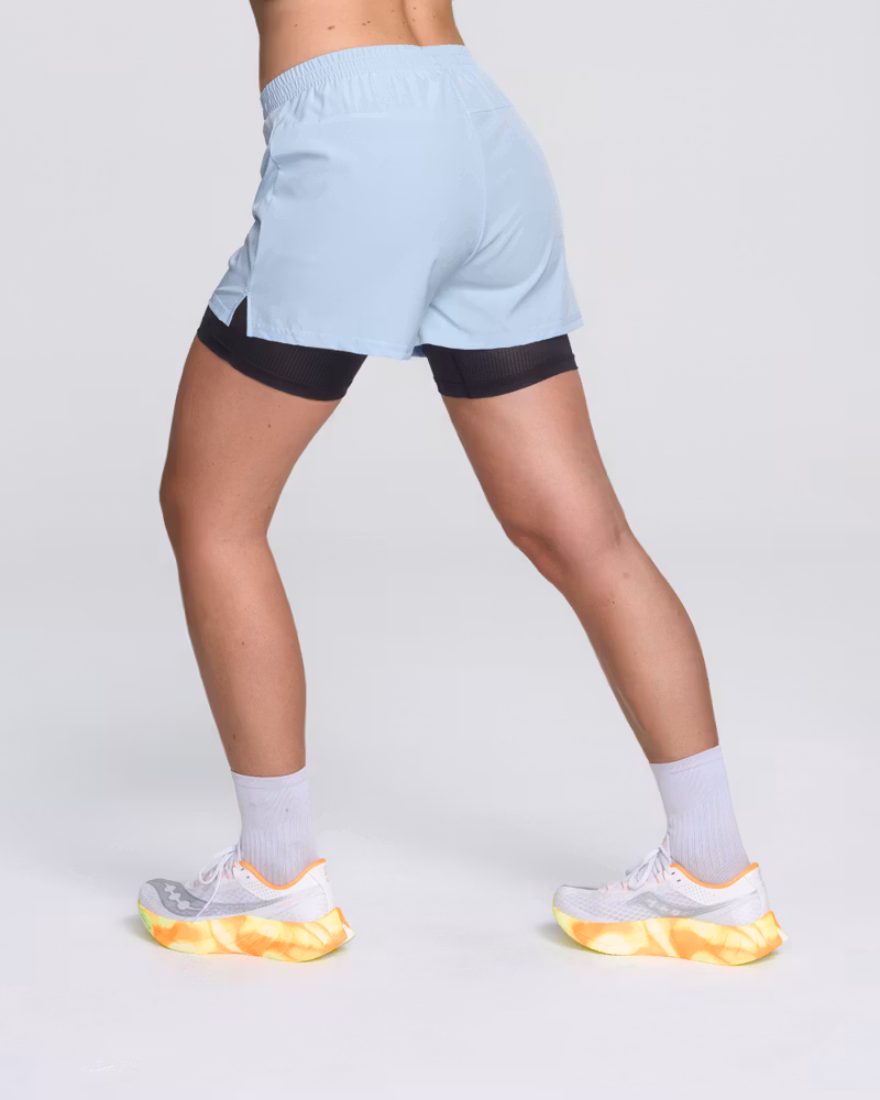 Back view of a woman running in Dæhlie's light blue 2-in-1 shorts, showcasing the active fit.