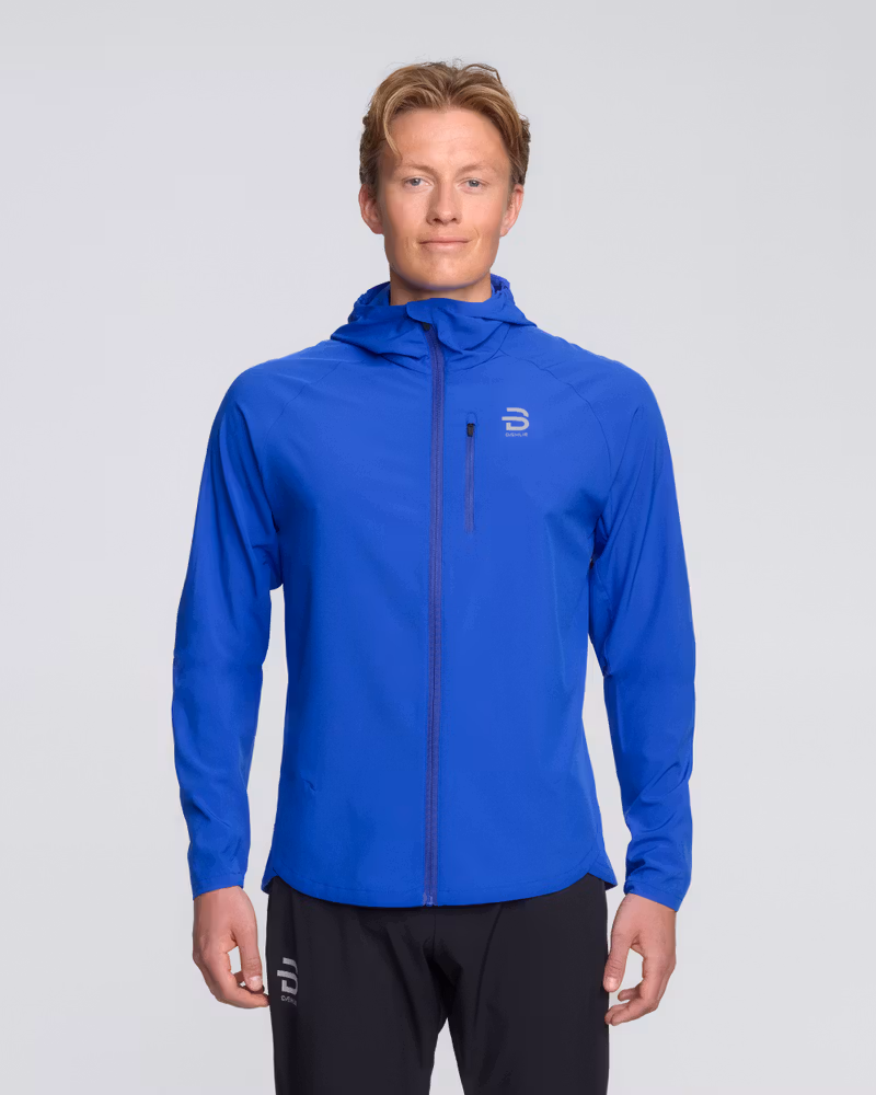 Male runner wearing the blue Dæhlie Jacket Run 2.0 with the hood up for light rain protection on a run.