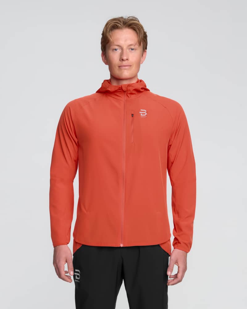 Front view of a runner in the Dæhlie red Jacket Run 2.0, featuring a protective fixed hood and chest pocket.