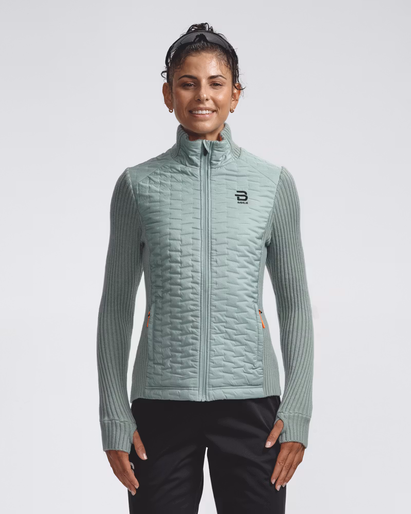 Woman wearing the light green Full Zip Comfy women's jacket, showing its wind-resistant quilted front and zippered pockets.
