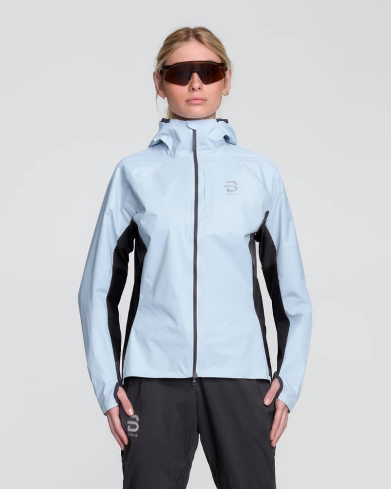 Runner wearing the women's Dæhlie Jacket Advance Light in light blue and black for high-intensity running in challenging weather.