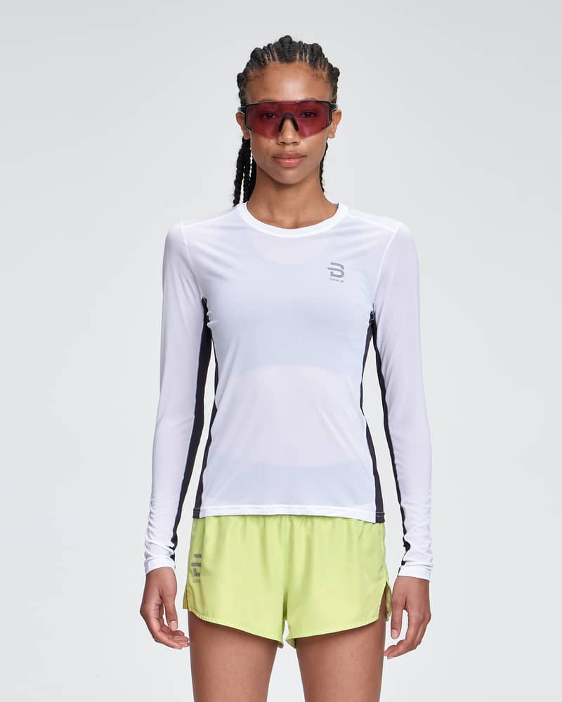 Woman running in the white and black Dæhlie Long Sleeve Air, featuring reflective details for visibility.