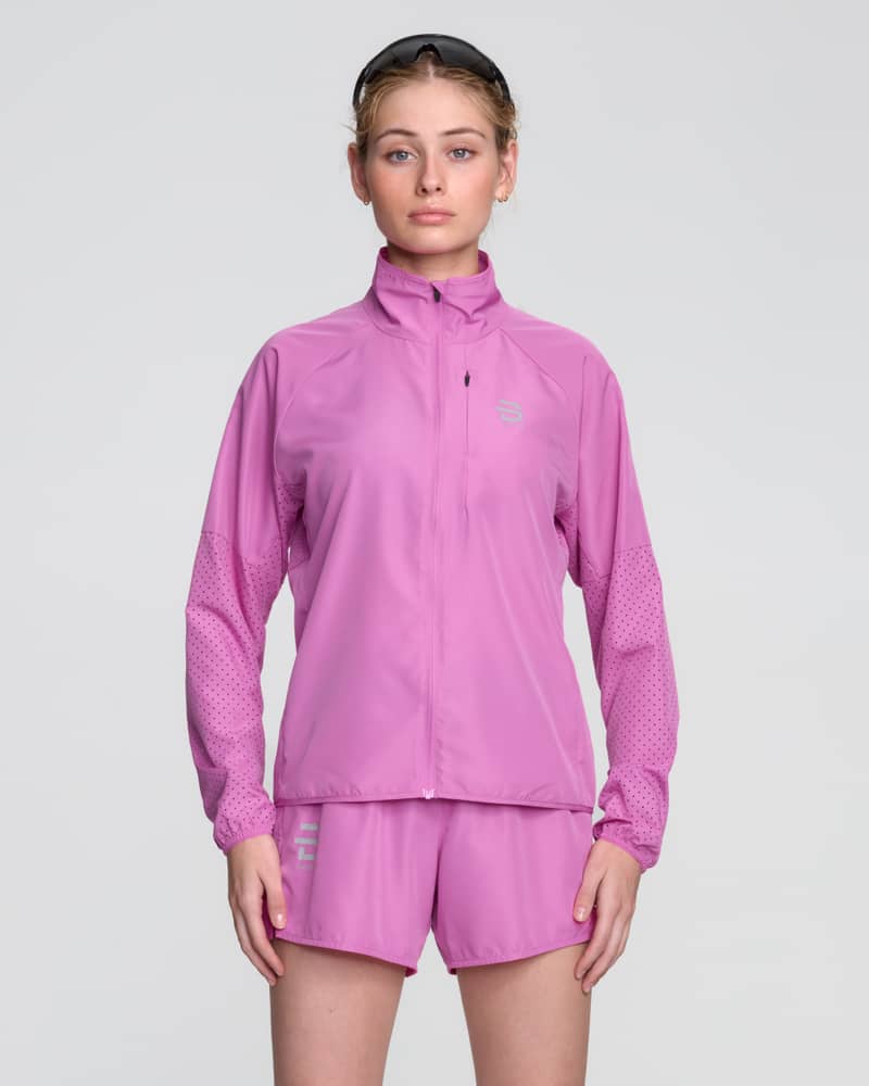 Female runner in the pink Dæhlie Jacket Air, a vibrant and lightweight jacket for warm weather workouts.