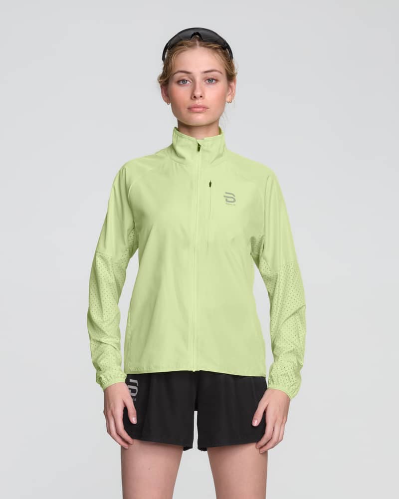 Woman in a light green Dæhlie running Jacket Air, a performance jacket with elastic cuffs for comfort.