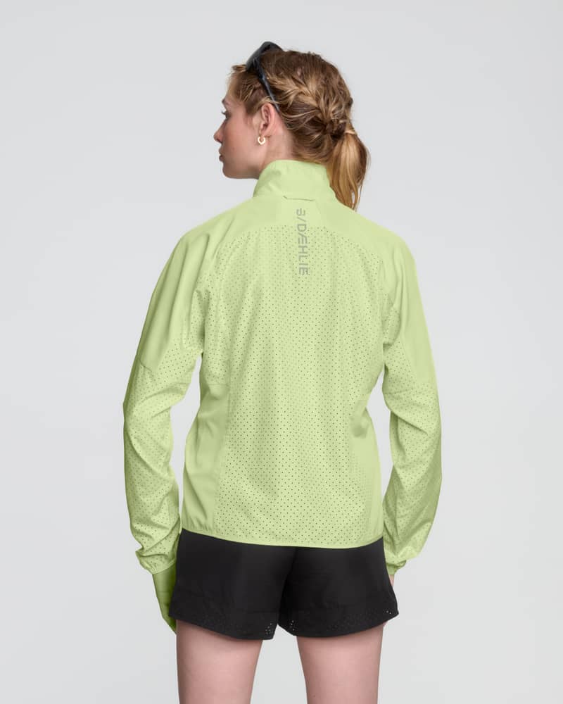 Rear view of a woman wearing the light green Dæhlie Jacket Air, showing its lightweight and functional design.