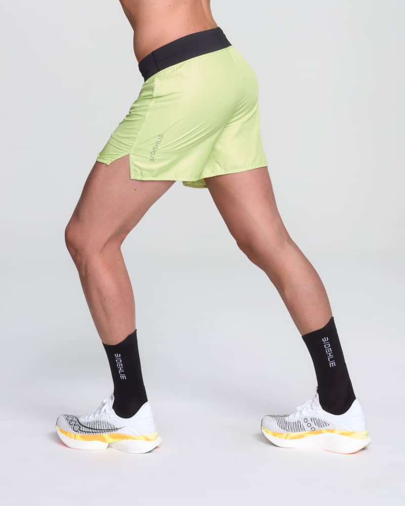 Back view of a runner in Dæhlie's lightweight lime green 5-inch running shorts, showing the split hem for mobility.
