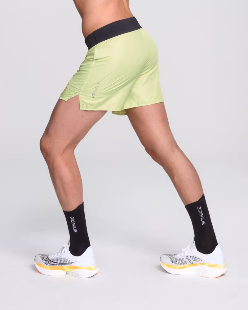 Back view of a runner in Dæhlie's lightweight lime green 5-inch running shorts, showing the split hem for mobility.