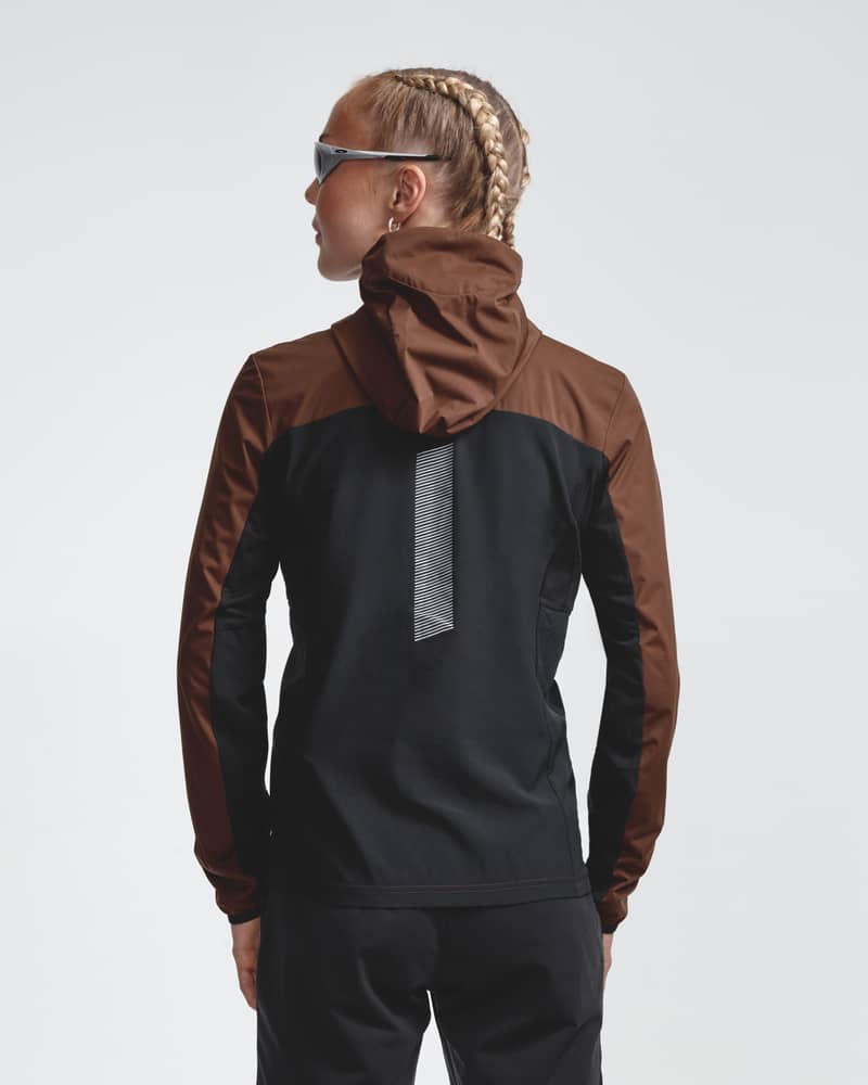 Rear view of a model wearing the brown Jacket Winter Run Protect, featuring a black back panel and a vertical reflective stripe for safety.