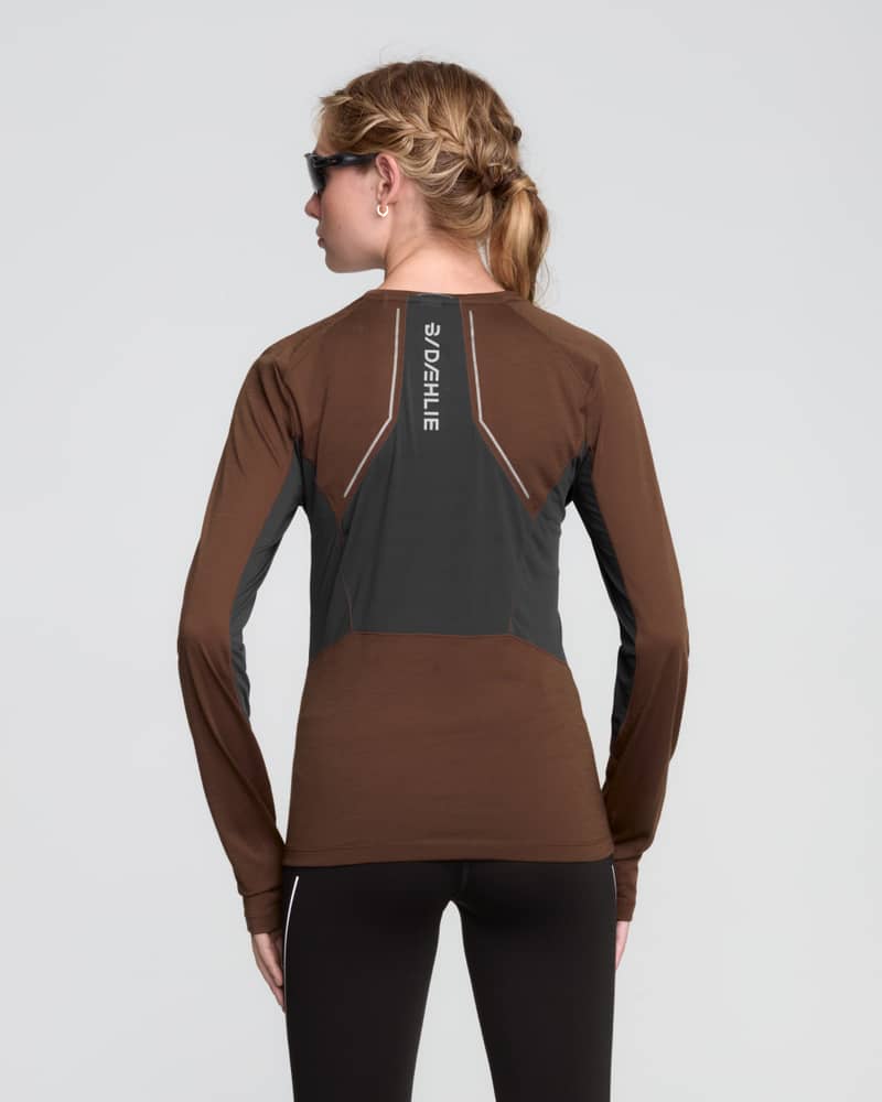 Rear view of a woman wearing the brown Dæhlie Long Sleeve Tech Wool with reflective details for visibility.