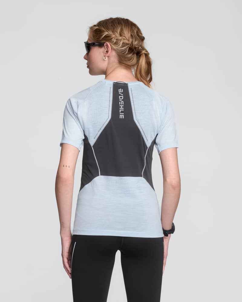Back of a female runner in a light blue Dæhlie tech wool tee, showing the strategically placed ventilation panel.
