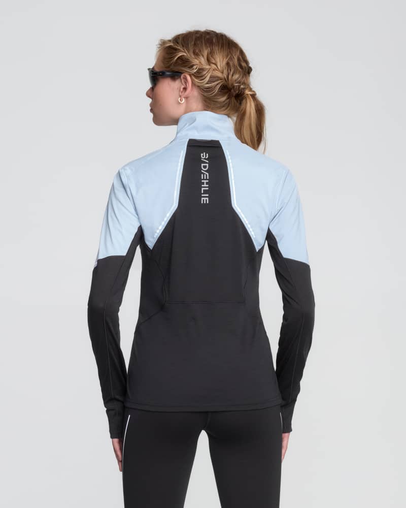 Back of a woman in a light blue Dæhlie tech wool half-zip, showcasing the reflective logo for safety.