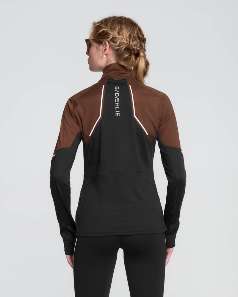 Rear view of a female runner in the brown and dark grey Dæhlie Half Zip Tech Wool, a midlayer with 360-degree reflective details.