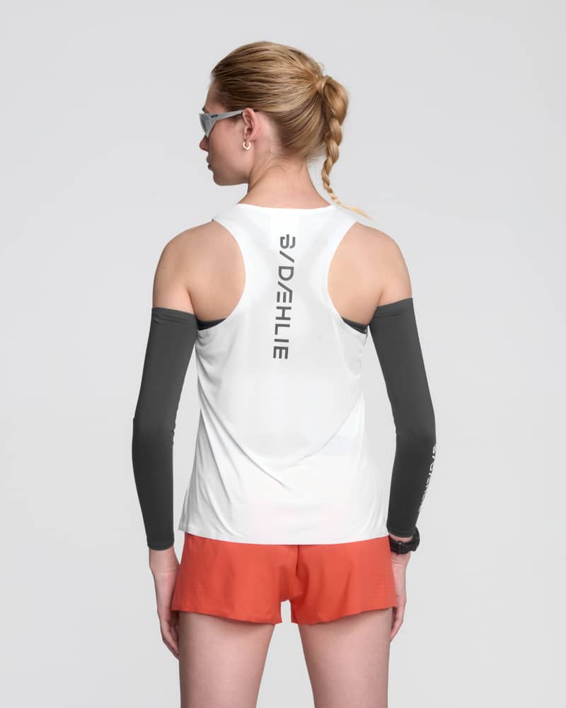 Female model wearing white Dæhlie racerback tank top with dark arm sleeves and orange shorts, back view