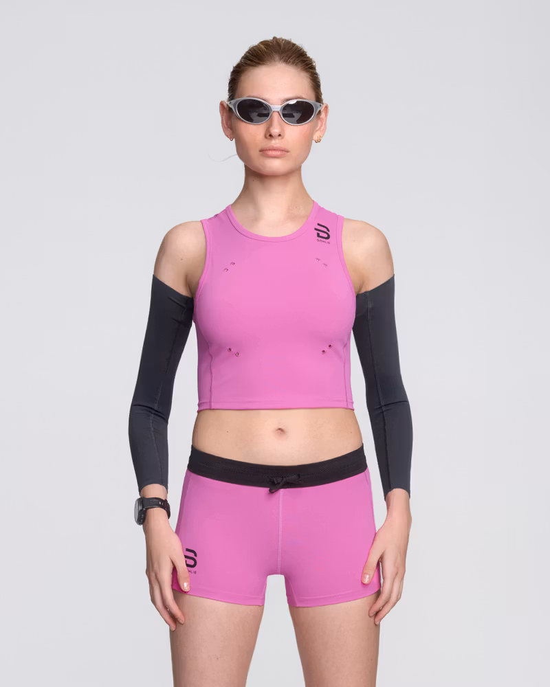 Female runner wearing Dæhlie's pink Top Elite running top, matched up with black Elite arm Sleeves, designed for race-day performance.