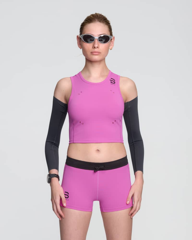 Female runner wearing Dæhlie's pink Top Elite running top, matched up with black Elite arm Sleeves, designed for race-day performance.
