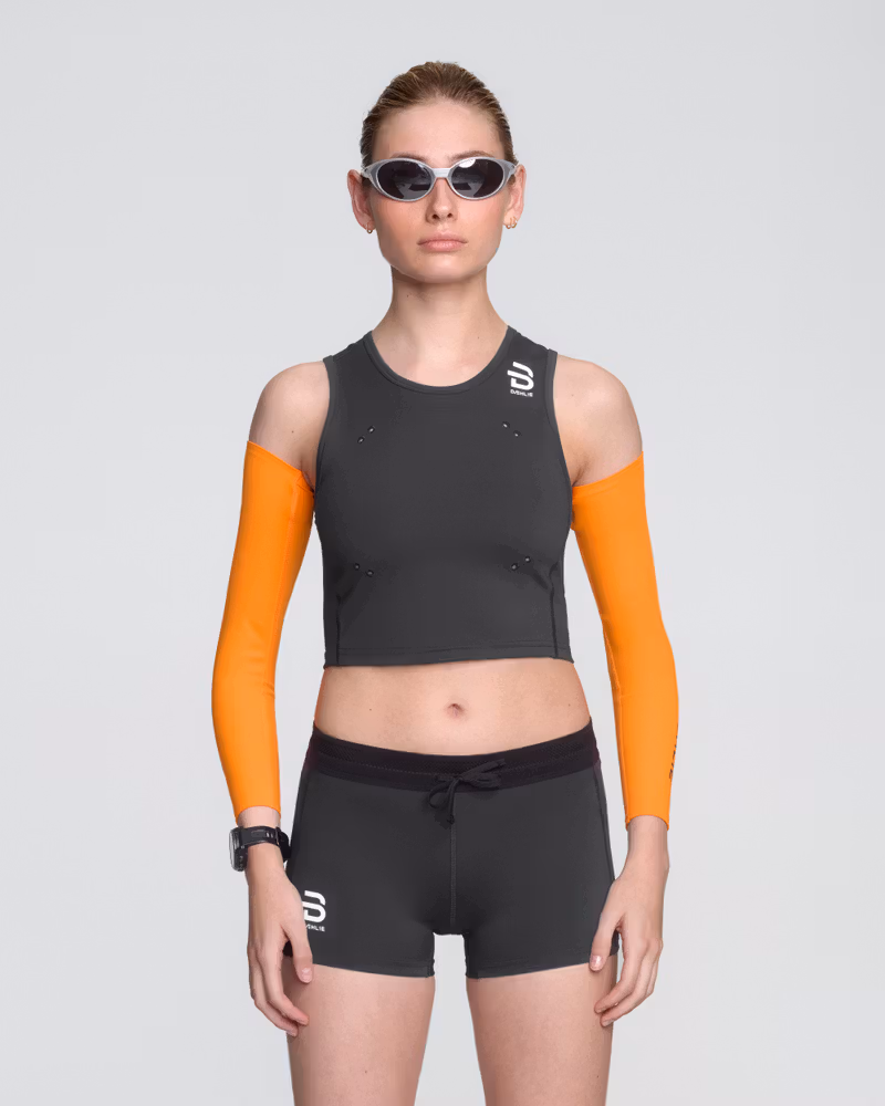 Runner in a Dæhlie black Top Elite for women, matched up with orange Elite arm Sleeves for a sleek look and high-performance features.