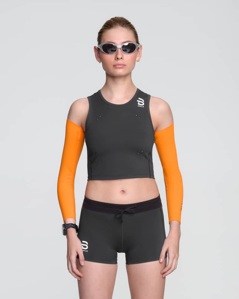 Runner in a Dæhlie black Top Elite for women, matched up with orange Elite arm Sleeves for a sleek look and high-performance features.