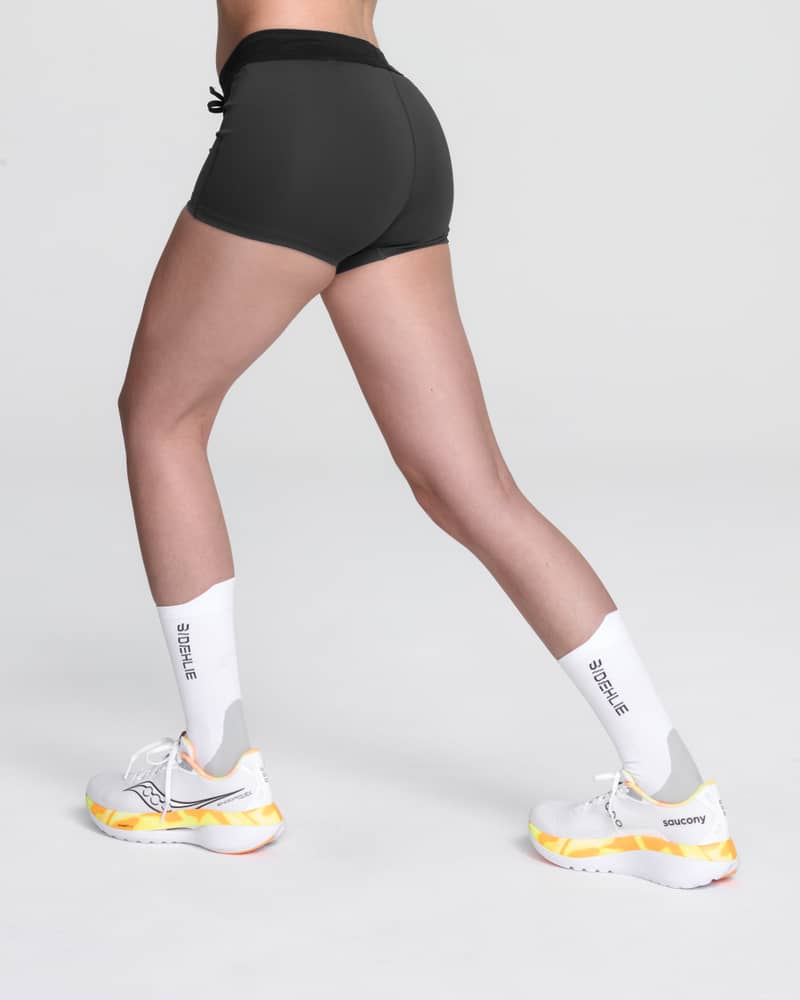 Studio shot of a runner in Dæhlie's black Elite Tights for women, showing the silicone grip at the hem to keep them in place.
