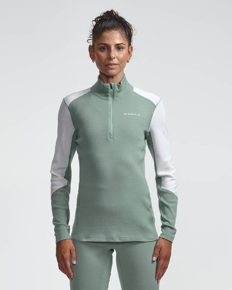 Dæhlie female model wearing sage green and white half-zip baselayer top, front view.