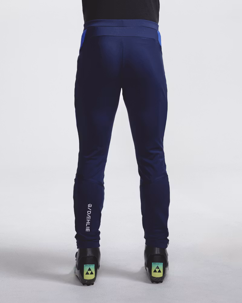 Rear full-length view of navy Dæhlie ski trousers with logo print and ski boots.