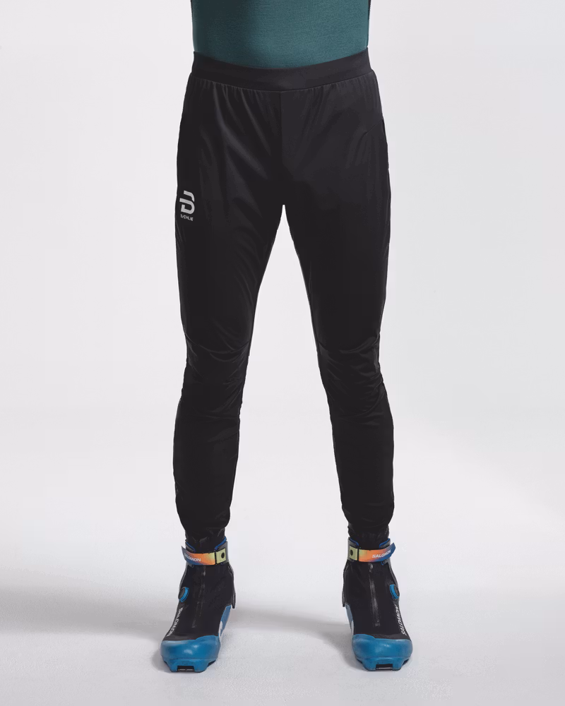 Front view of legs wearing black Dæhlie trousers with logo on the thigh and ski boots.