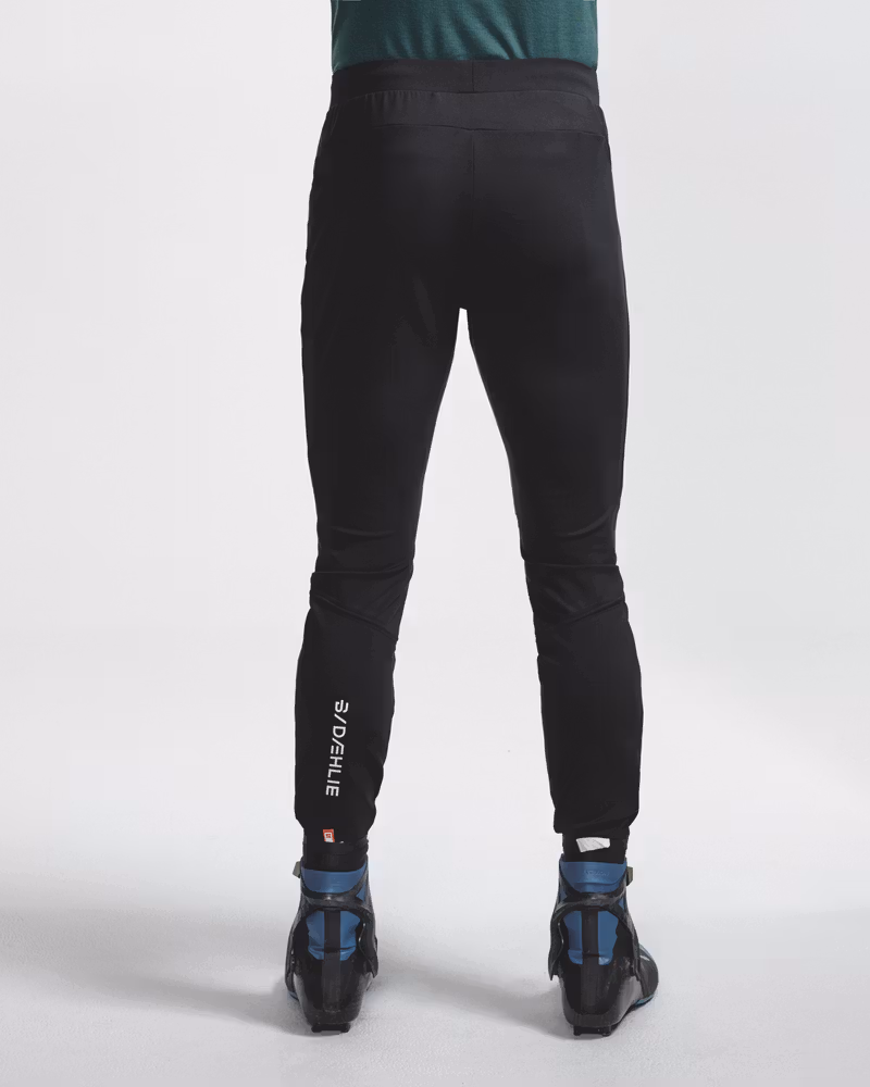 Rear view of legs wearing black Dæhlie trousers with logo print and ski boots.